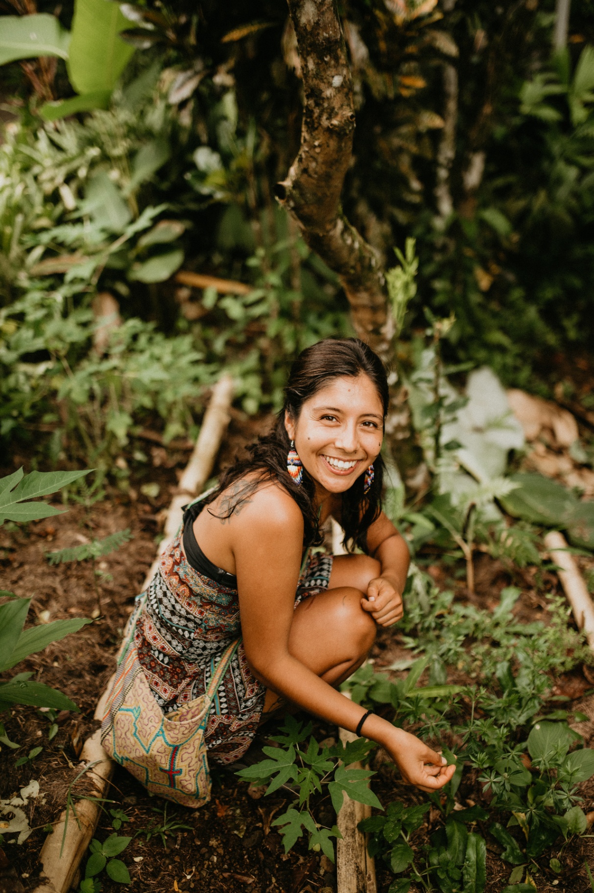 Indigenous woman smiling while tending plants in a lush forest garden